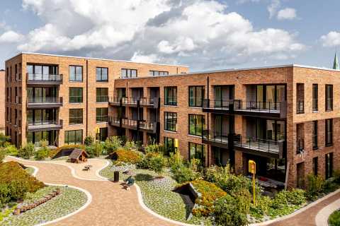 Modernes Wohnhaus aus Klinker mit begrüntem Innenhof unter blauem Himmel.