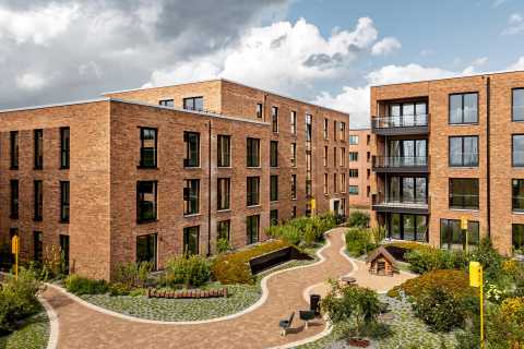 Moderne Wohngebäude aus Backstein mit begrüntem Innenhof und Sitzbänken.