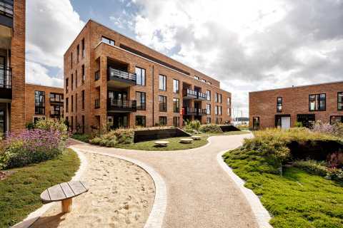Moderne Backsteinwohngebäude mit Balkonen und begrüntem Innenhof bei Tageslicht.
