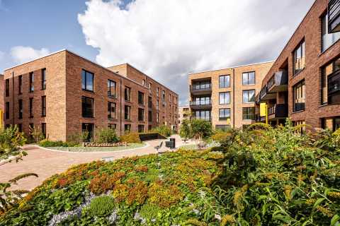 Moderne Wohngebäude aus Backstein mit begrüntem Innenhof und Sitzbänken.