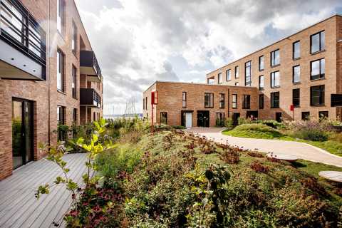 Neue Backsteingebäude mit großen Fenstern und begrüntem Innenhof bei Sonne.