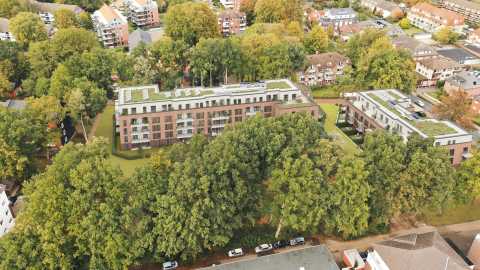 Luftbild von modernen Mehrfamilienhäusern mit Flachdach, umgeben von Bäumen.