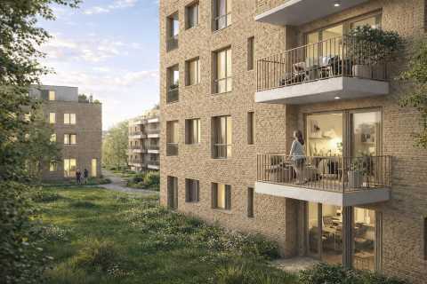 Frau steht auf Balkon eines modernen Wohnhauses, grüne Wiese davor.