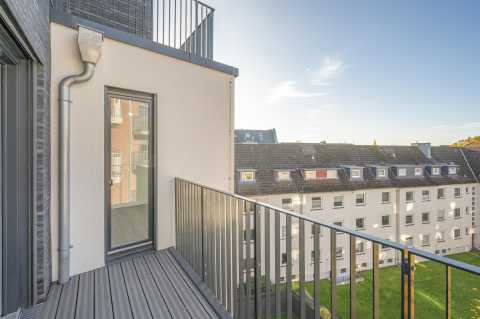 Kleiner Balkon mit grauem Geländer, Blick auf Nachbarhäuser und blauen Himmel.