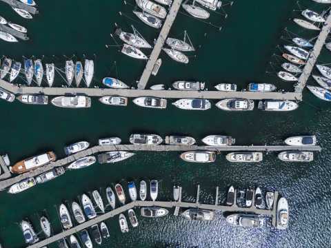 Viele Boote und Yachten liegen an Stegen in einem Hafen, von oben fotografiert.