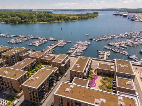 Moderne Wohnhäuser mit begrünten Dächern am Yachthafen an einem See.
