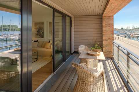 Balkon mit Blick auf einen Yachthafen, zwei Korbstühle und ein Holztisch