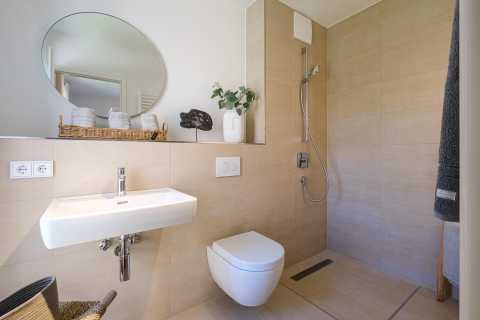 Modernes, helles Bad mit Hänge-WC, Waschbecken und bodengleicher Dusche.