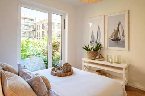 Helles Schlafzimmer mit Doppelbett, Fenster, Pflanzen und Segelboot-Bildern an der Wand.