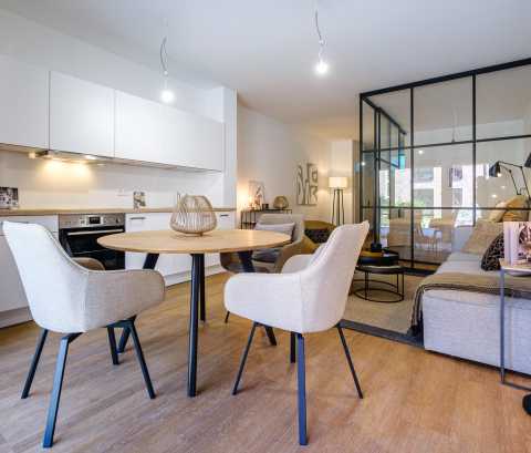Helle, moderne Wohnküche mit Esstisch, Sessel und Glaswand zum Wohnzimmer.