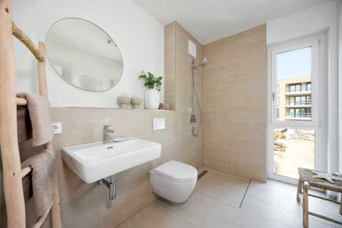 Modernes, helles Bad mit ebenerdiger Dusche, WC, Waschbecken und Fenster.