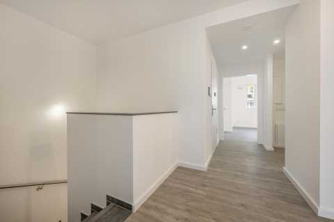 Heller Flur mit Holzfußboden, Treppenabgang und Blick in ein weiteres Zimmer.