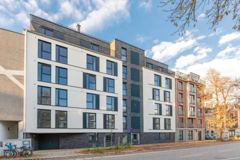 Modernes mehrstöckiges Wohngebäude mit großen Fenstern an einer Straße.