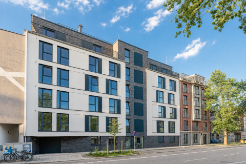 Modernes mehrstöckiges Wohnhaus mit großen Fenstern an einer Straße.
