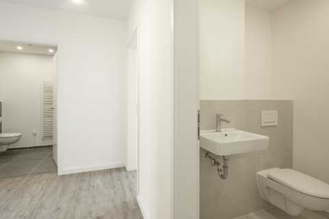 Modernes, helles Bad mit Wand-WC, Waschbecken und grauem Fliesenboden.