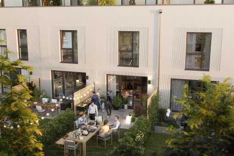 Mehrere Menschen sitzen und stehen im Garten vor modernen Reihenhäusern.