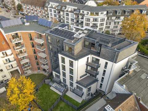 Mehrstöckiges Wohnhaus mit Balkonen, Solaranlagen und begrüntem Innenhof.