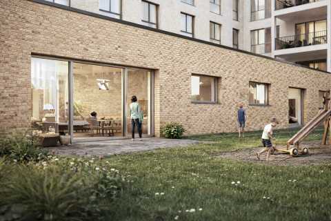 Kinder spielen auf einer Wiese vor einem Backsteingebäude mit großen Fenstern.