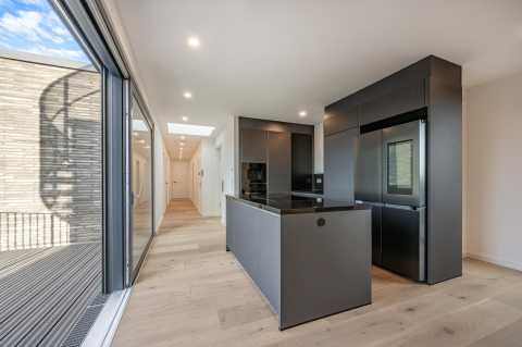 Moderne Küche mit schwarzer Einrichtung, Insel und großem Fenster zum Balkon.