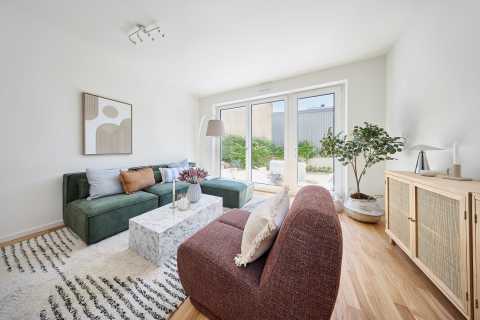 Modernes Wohnzimmer mit großen Fenstern, Pflanzen und gemütlicher Einrichtung.