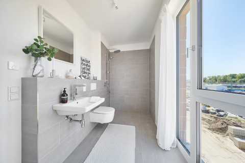 Modernes, helles Badezimmer mit bodengleicher Dusche, WC, Waschbecken und Fenster.