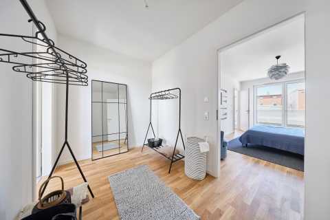Heller Flur mit Garderobe, Spiegel und Blick in ein Schlafzimmer mit Balkon.