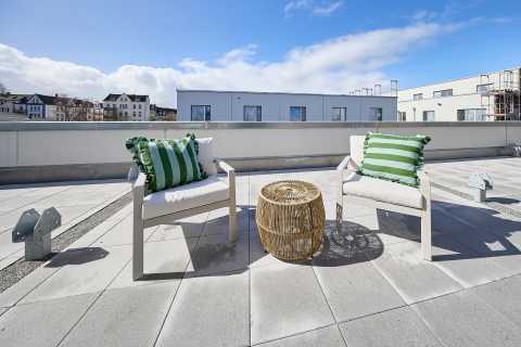 Zwei Stühle mit grünen Kissen und kleinem Tisch auf einer Dachterrasse.