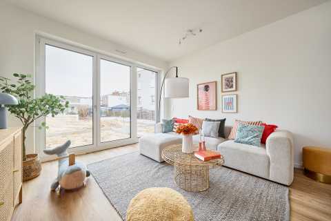 Helles Wohnzimmer mit Sofa, Couchtisch, großer Fensterfront und Dekokissen.