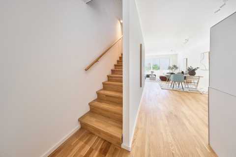 Helle Diele mit Holztreppe links und offenem Wohn- und Essbereich rechts.