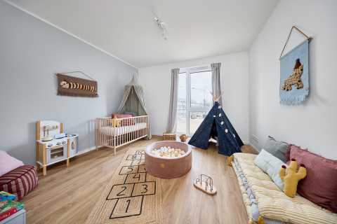 Helles Kinderzimmer mit Tipi, Bällebad, Teppich und Spielküche auf Holzboden.