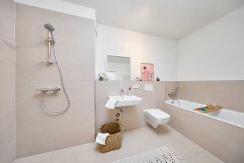 Modernes, helles Bad mit Dusche, Badewanne, WC, Waschbecken und Korb.