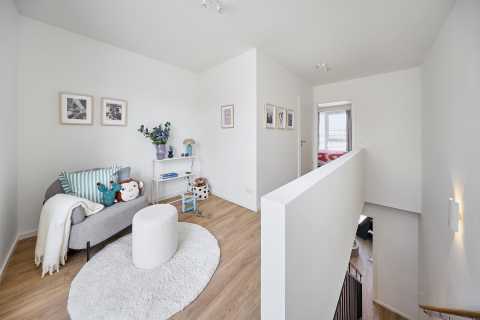 Heller Flur mit Sitzecke, Bildern, Spielzeug, Teppich und Schlafzimmer im Hintergrund.