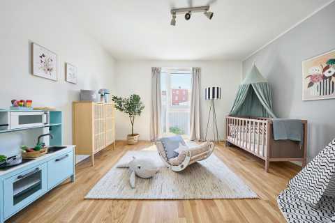 Helles Kinderzimmer mit Holzfußboden, Spielküche, Gitterbett und Spielzeug.