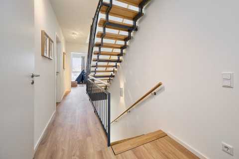 Moderner Flur mit Holztreppe, Handlauf und hellem Holzboden.