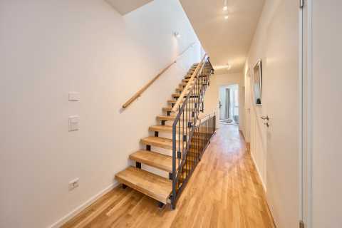 Moderner Flur mit Holztreppe, Handlauf und hellem Holzboden, Türen seitlich