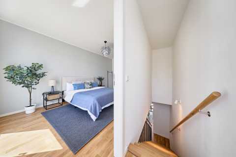 Modernes Schlafzimmer mit Doppelbett, Pflanze und Treppe im Flur rechts.