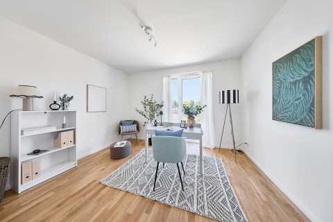 Modernes, helles Arbeitszimmer mit Schreibtisch, Sessel und großen Fenstern.