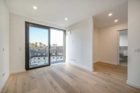 Helles Zimmer mit Holzfußboden, Balkonzugang und Blick ins moderne Bad.