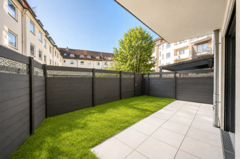 Kleine Terrasse mit Rasen, modernem Zaun und umliegenden Wohnhäusern.