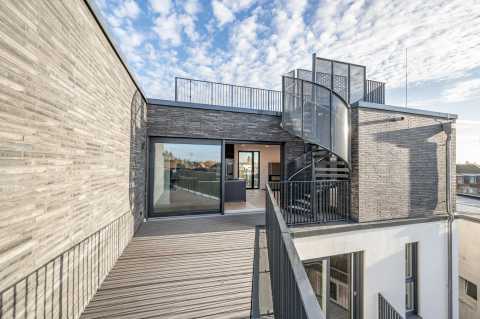 Moderne Dachterrasse mit Holzbelag und Wendeltreppe unter blauem Himmel.