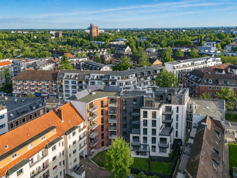 Luftaufnahme von Wohngebäuden mit viel Grün und blauem Himmel im Hintergrund.