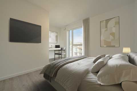 Modernes Schlafzimmer mit Bett, TV, Schreibtisch und großem Fenster mit Vorhang.