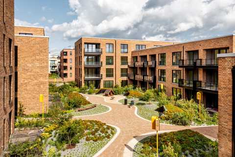 Moderner Innenhof mit Wegen, Bänken, Grünflächen und umgebenden Wohnhäusern.